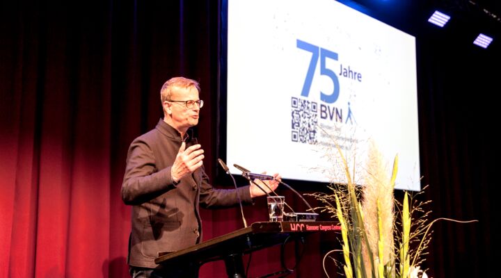 Volker Bajus ist groß, schlank, trägt eine Brille, ein modisches Jackett zur Jeanshose. Er bewegt die Arme zu einer ausladenden Geste