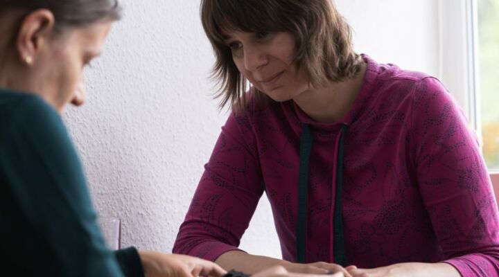 In der Beratung Zwei Frauen sind in einer Beratungssituation zu sehen. Sie sitzen an einem kleinen Tisch. Es liegen Münzen auf diesem. Sie wirken konzentriert.