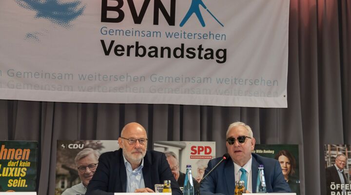 Andreas Kuhnt und Hans-Werner Lange sitzen am Podiumstisch. Kuhnt hat eine Glatze, einen kurzen weißen Vollbart, Brille, ein hellblaues Hemd, ein dunkles Sakko. Lange hat weiße Haare, Sonnenbrille, weißes Hemd, blaues Sakko, BVN-Krawatte.