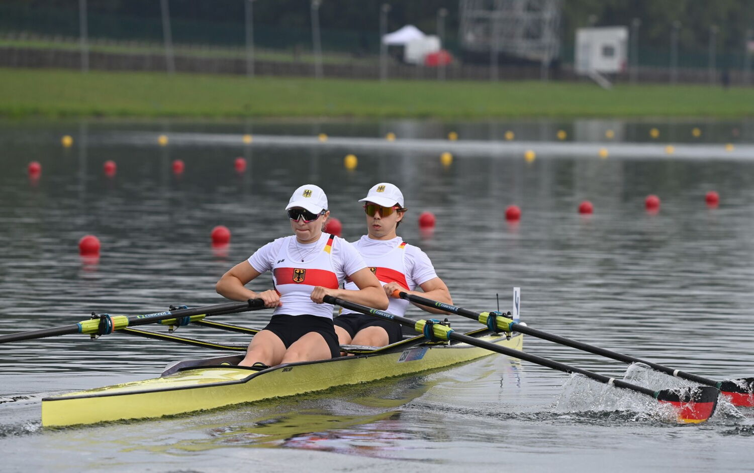Eine Frau und ein Mann sitzen in einem Ruderboot-Zweier und rudern angestrengt. Sie tragen ein Deutschland-Trikot, eine Brille und ein weißes Cappie.